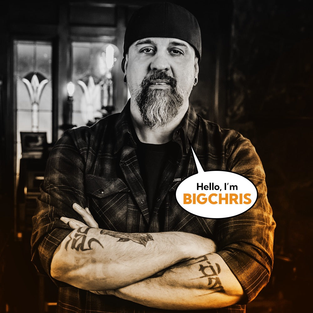 BigChris, Studio Director at Corvus Comics, confidently posing with tattooed arms crossed.
