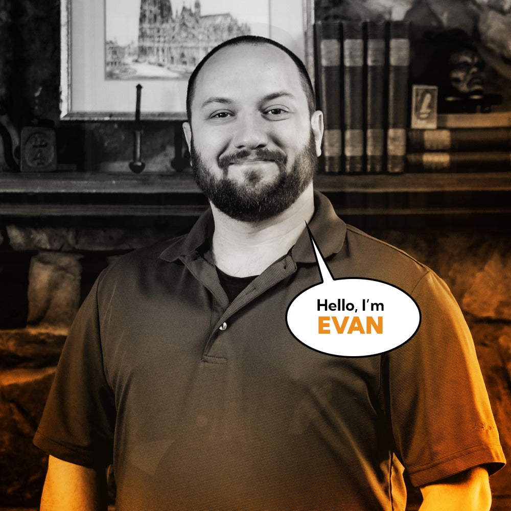 Portrait of Evan, team member at Corvus Comics, smiling warmly against an artistic backdrop with books and framed artwork, highlighting a welcoming and creative atmosphere.