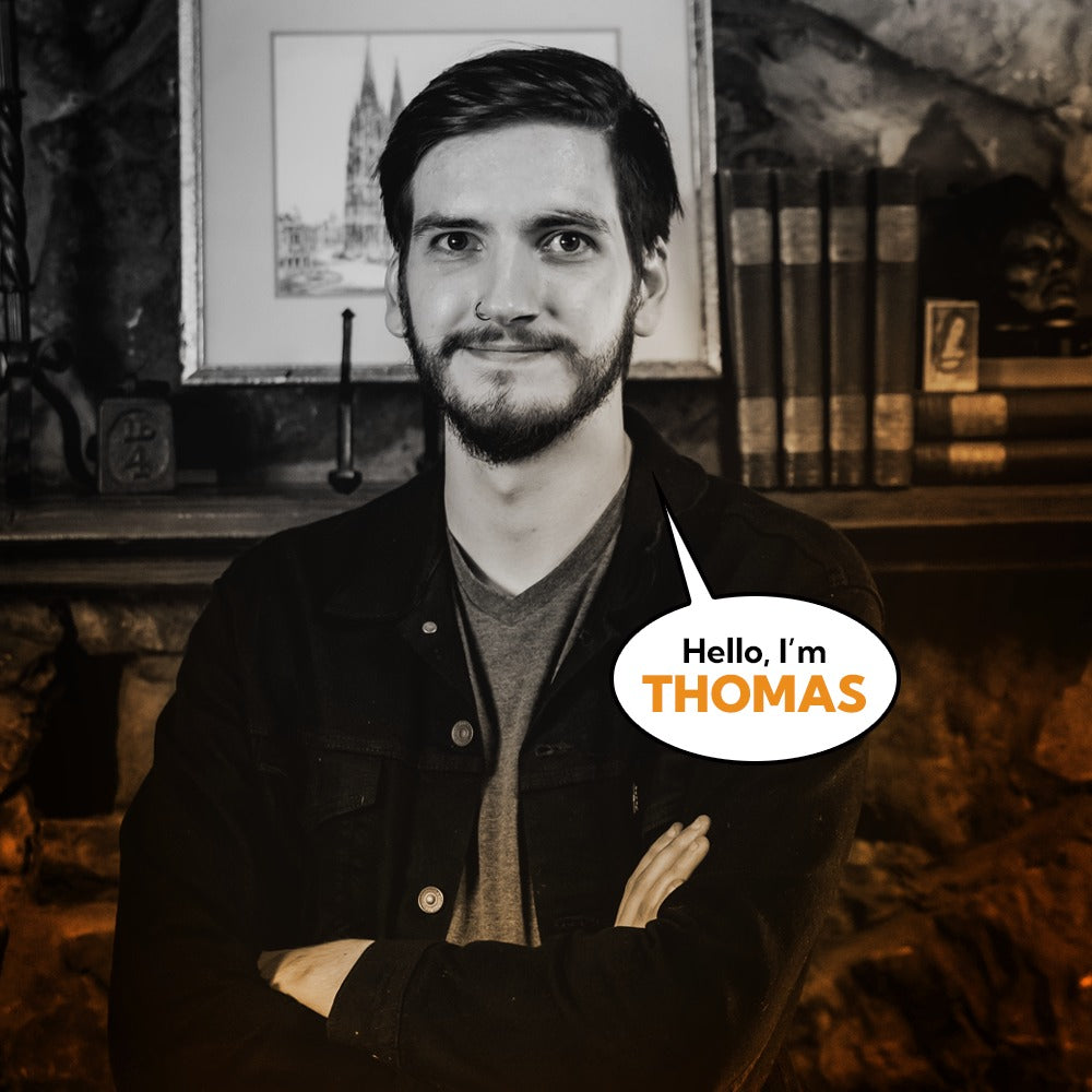 Portrait of Thomas Hedglen II, Lead Artist at Corvus Comics, smiling confidently with arms crossed, in a warmly lit, artistic studio setting.